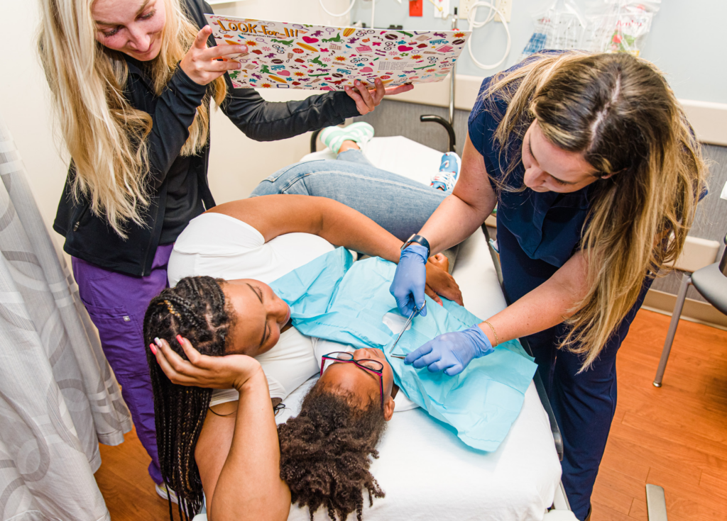 A child-life specialist and clinician using comfort positioning during a procedure